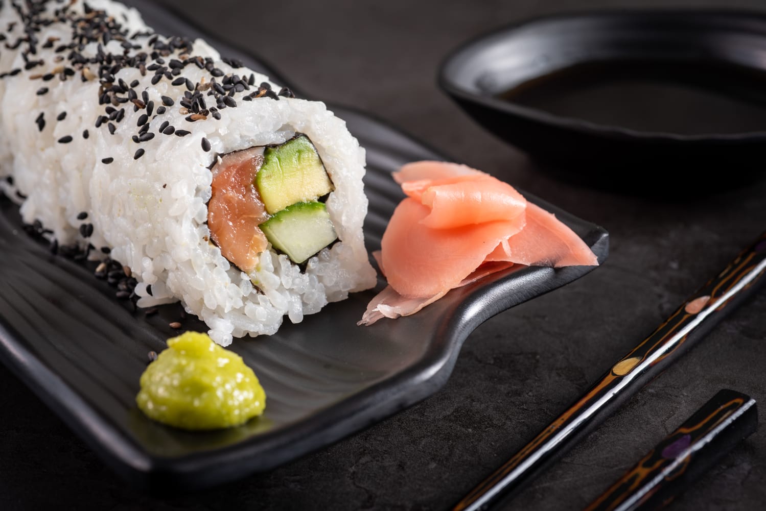 Sushi with tuna, avocado with wasabi and red cabbage on a slate plate with a black bowl containing soy sauce