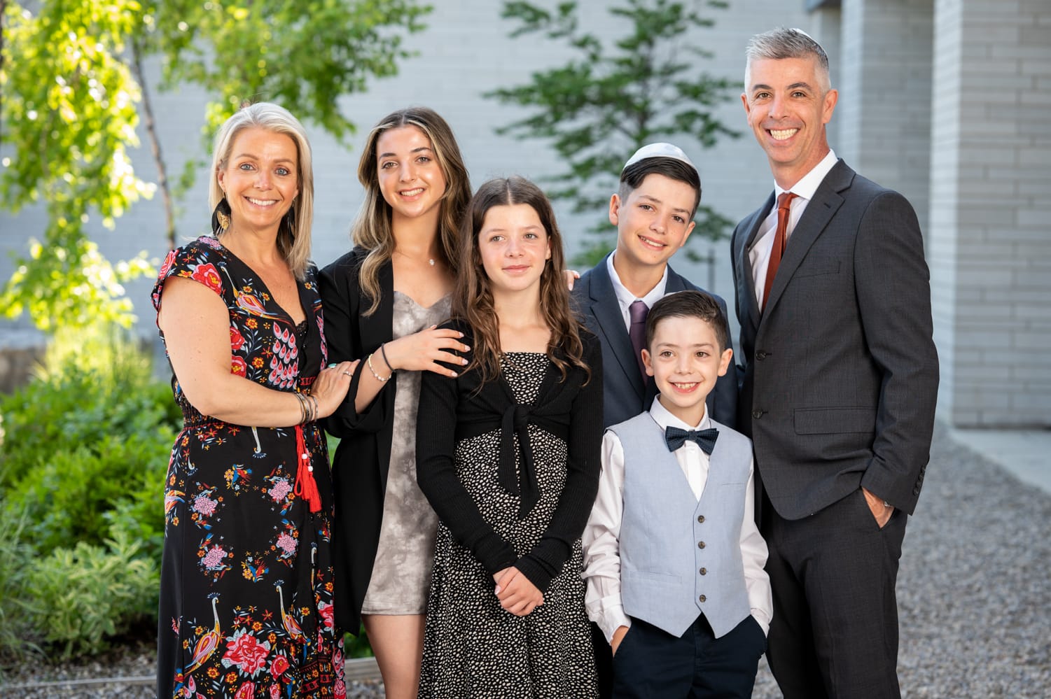 Bat mitzva girl with her her mother, father, sister and brothers smiling outside a grey synagogue